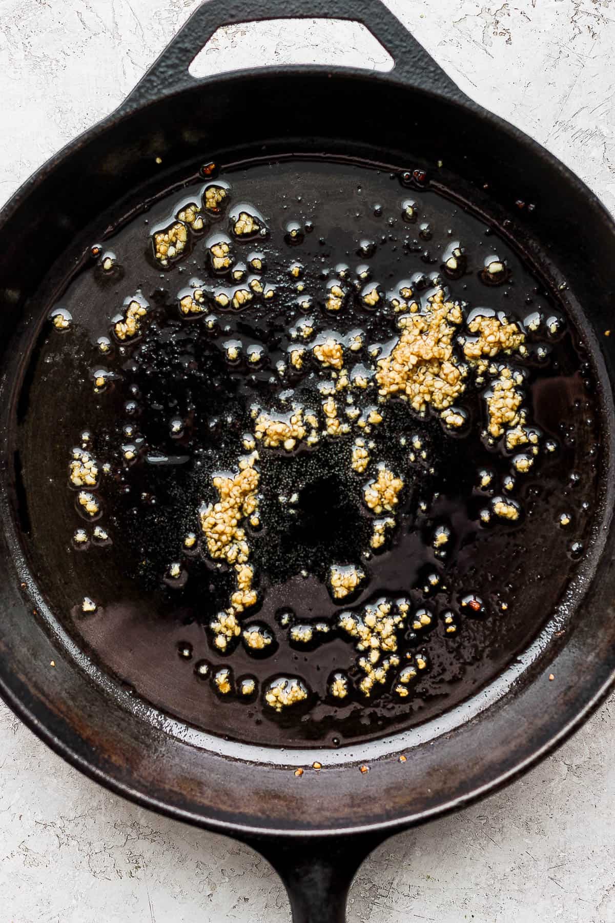 Garlic sautéing in olive oil on a skillet.