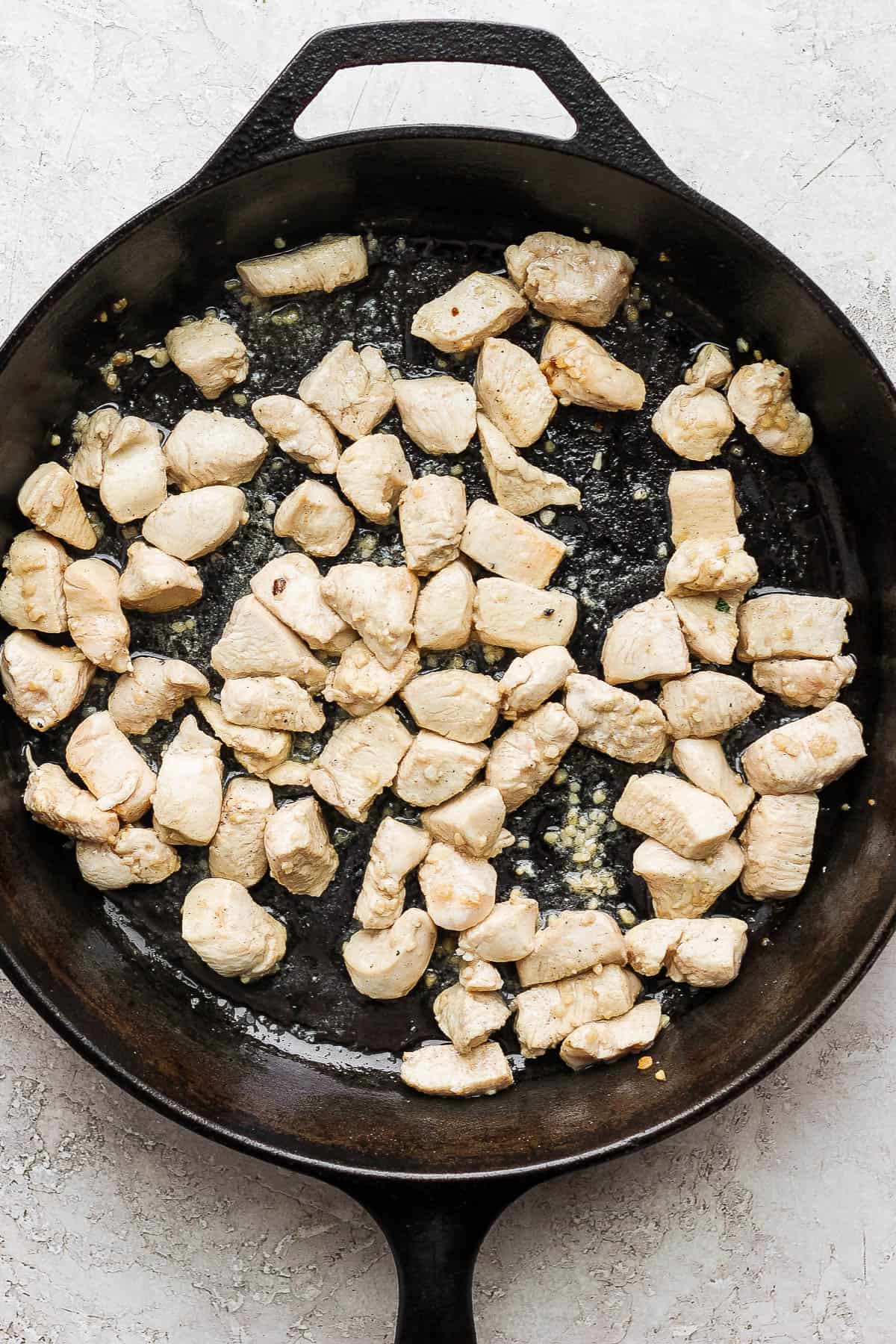 Cooked chunks of chicken in the cast iron skillet with the garlic.