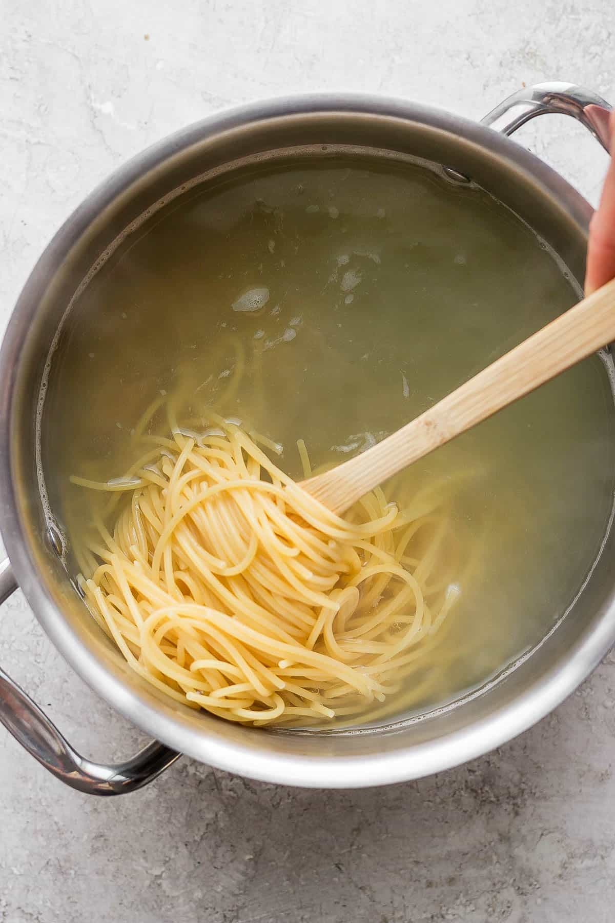 Spaghetti noodles cooking in a large pot and being pulled out with a wooden spoon.