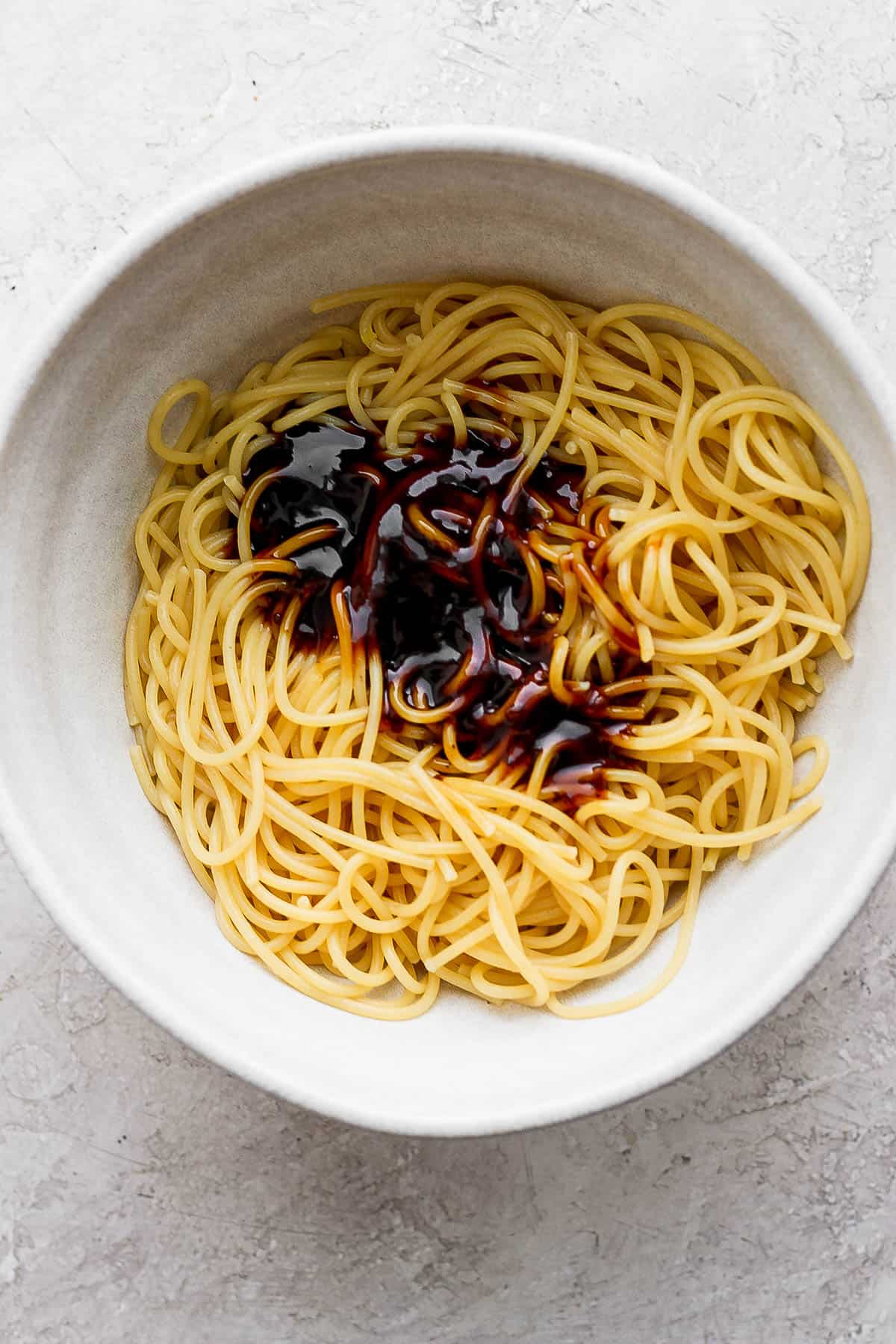 Cooked noodles in a large bowl with teriyaki sauce on top.
