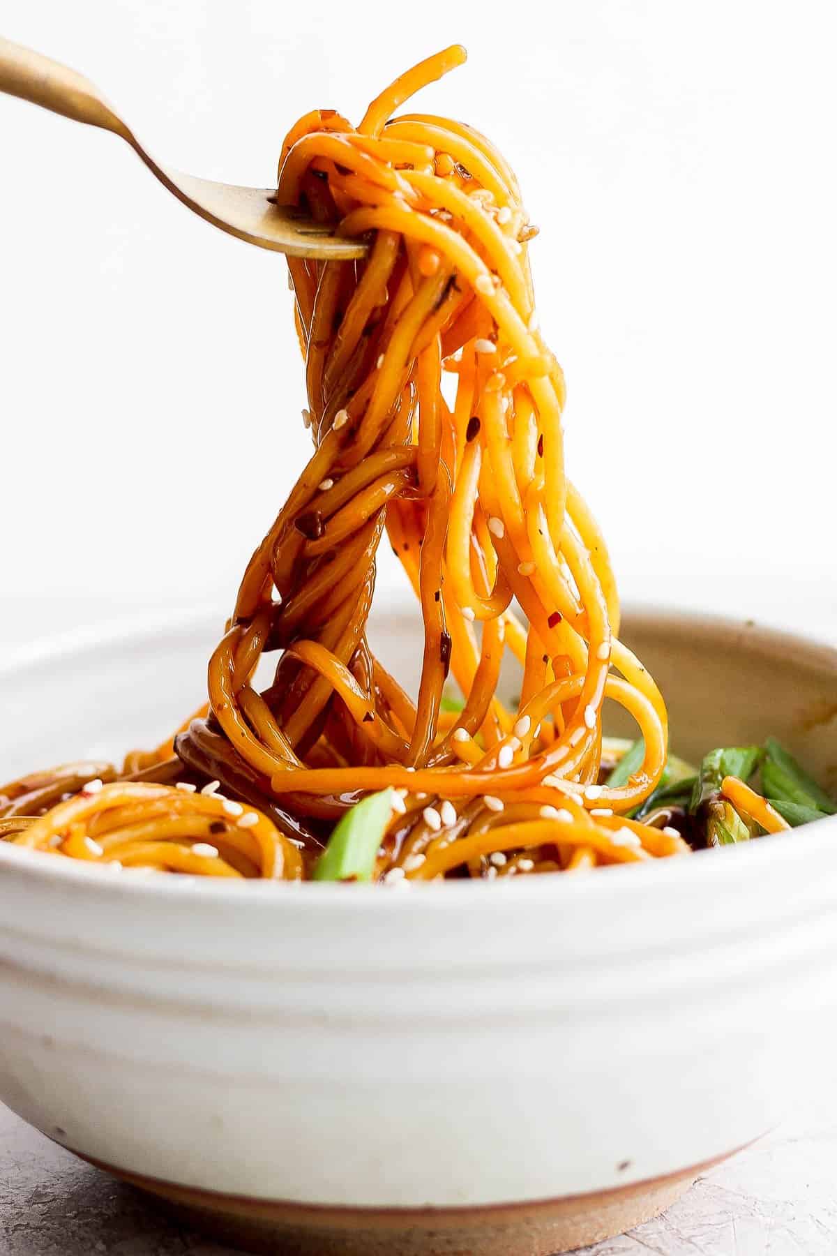 Teriyaki noodles being pulled out of a bowl with a fork.