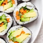 A plate of avocado sushi rolls cut into pieces with carrots, cilantro and cucumber.