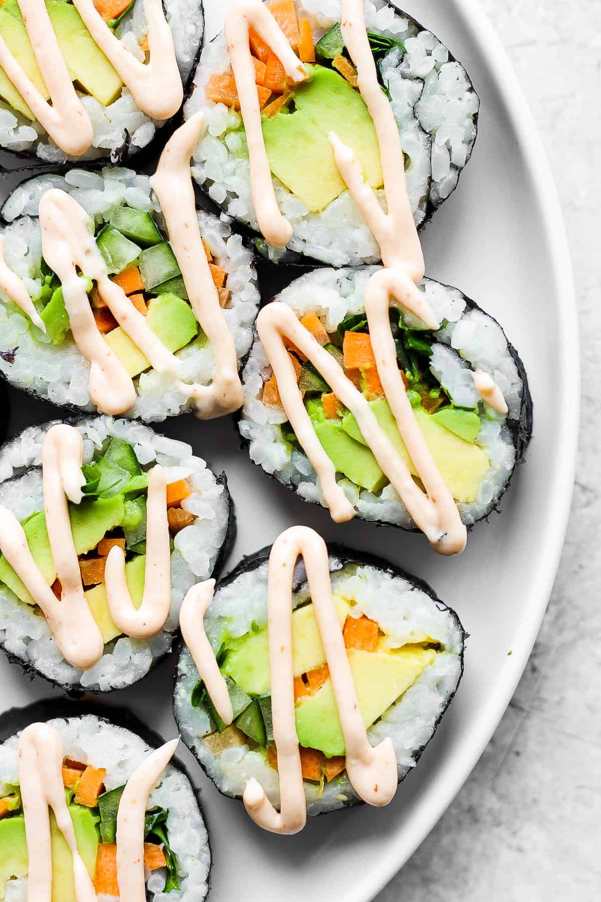 Pieces of an avocado roll on a white plate with a drizzle of spicy mayo on top.