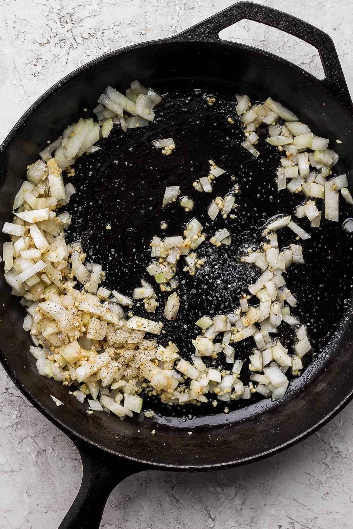 Onions and garlic being sauteed in a cast iron skillet. 