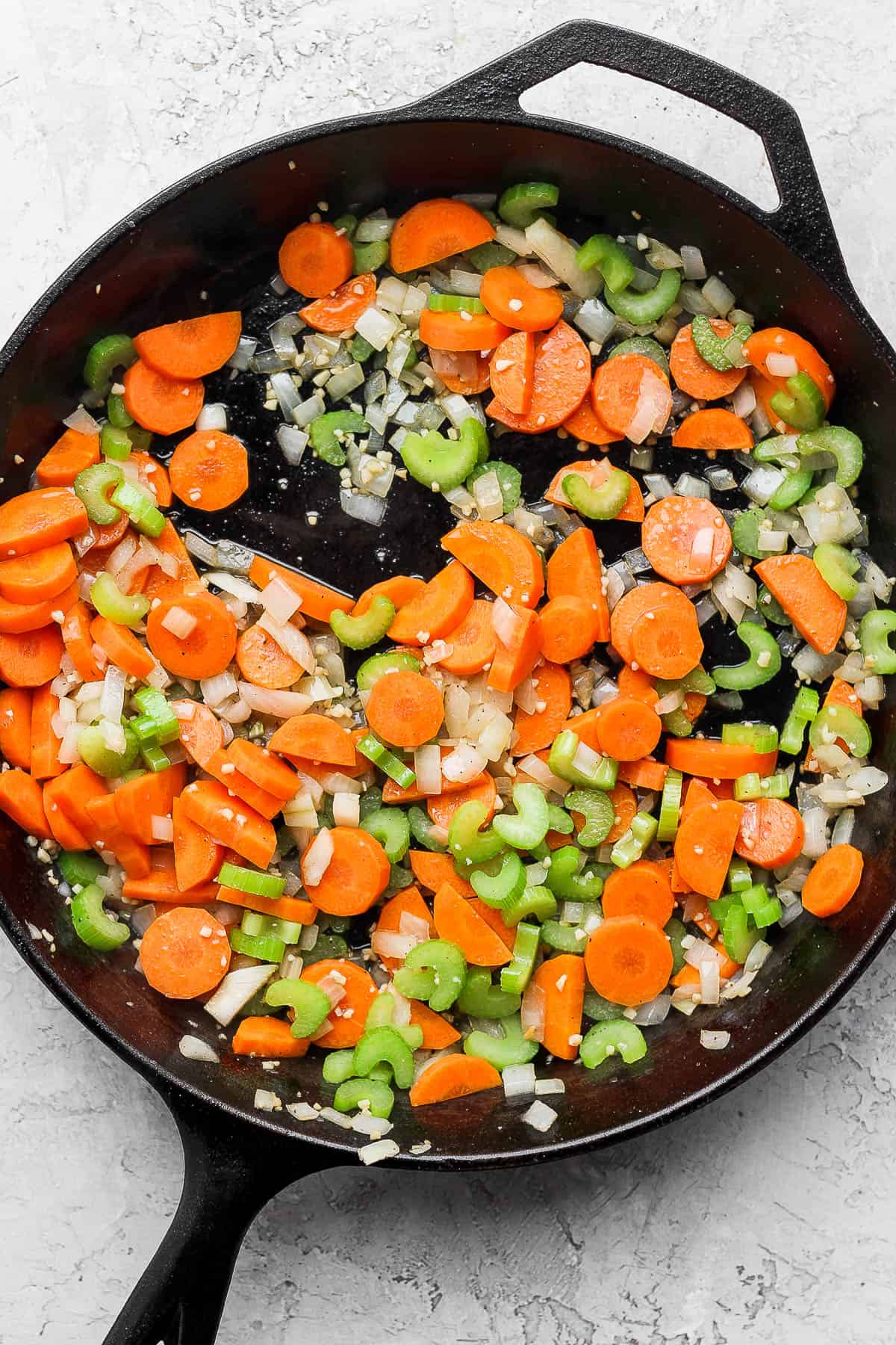Carrots and celery are added to the cast iron skillet. 