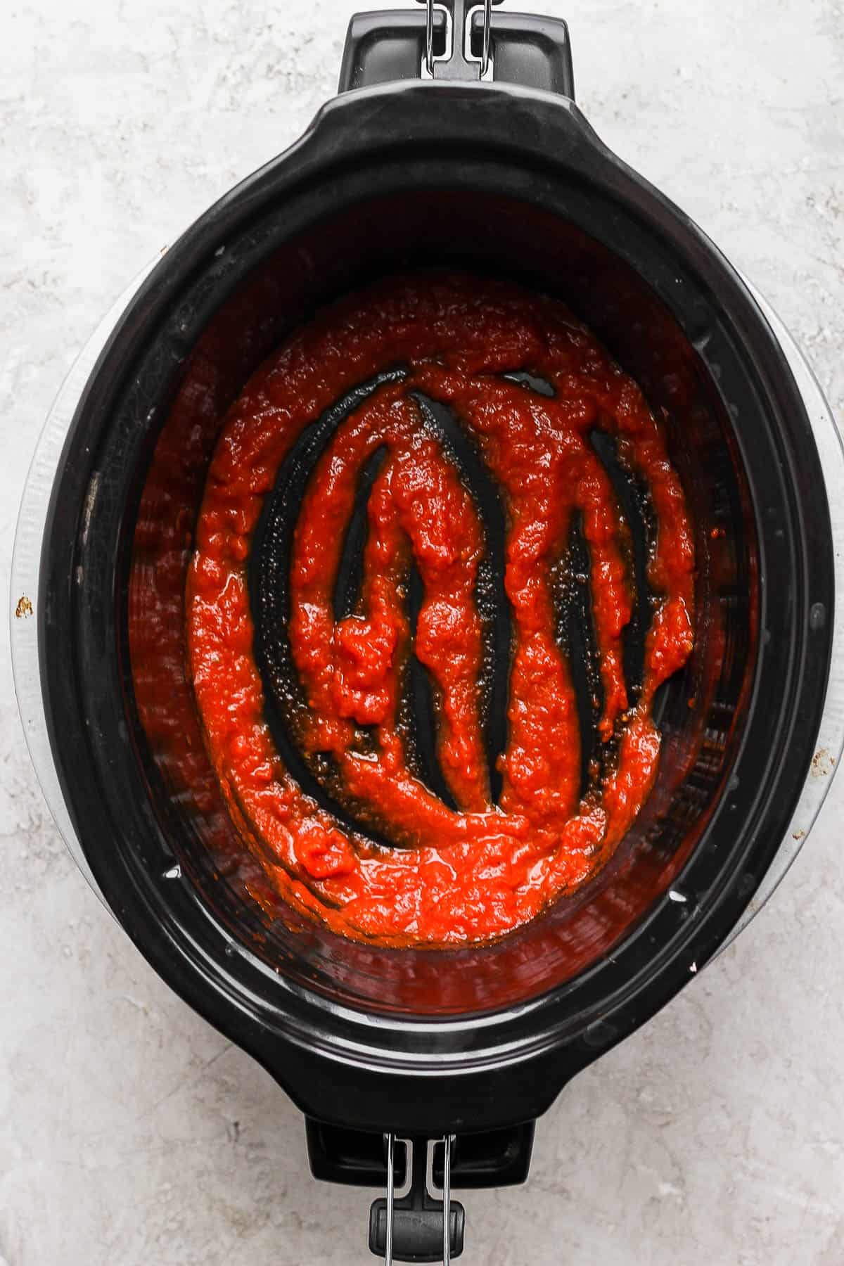 A slow cooker with just some marinara in the bottom.