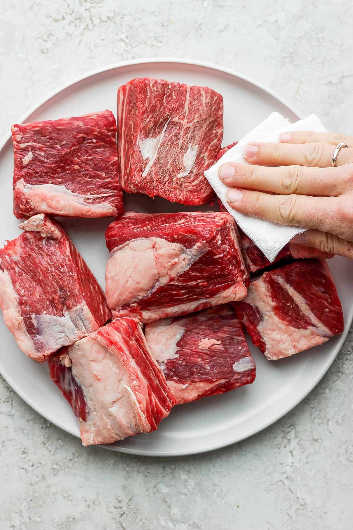 Someone patting dry a plate of short ribs.