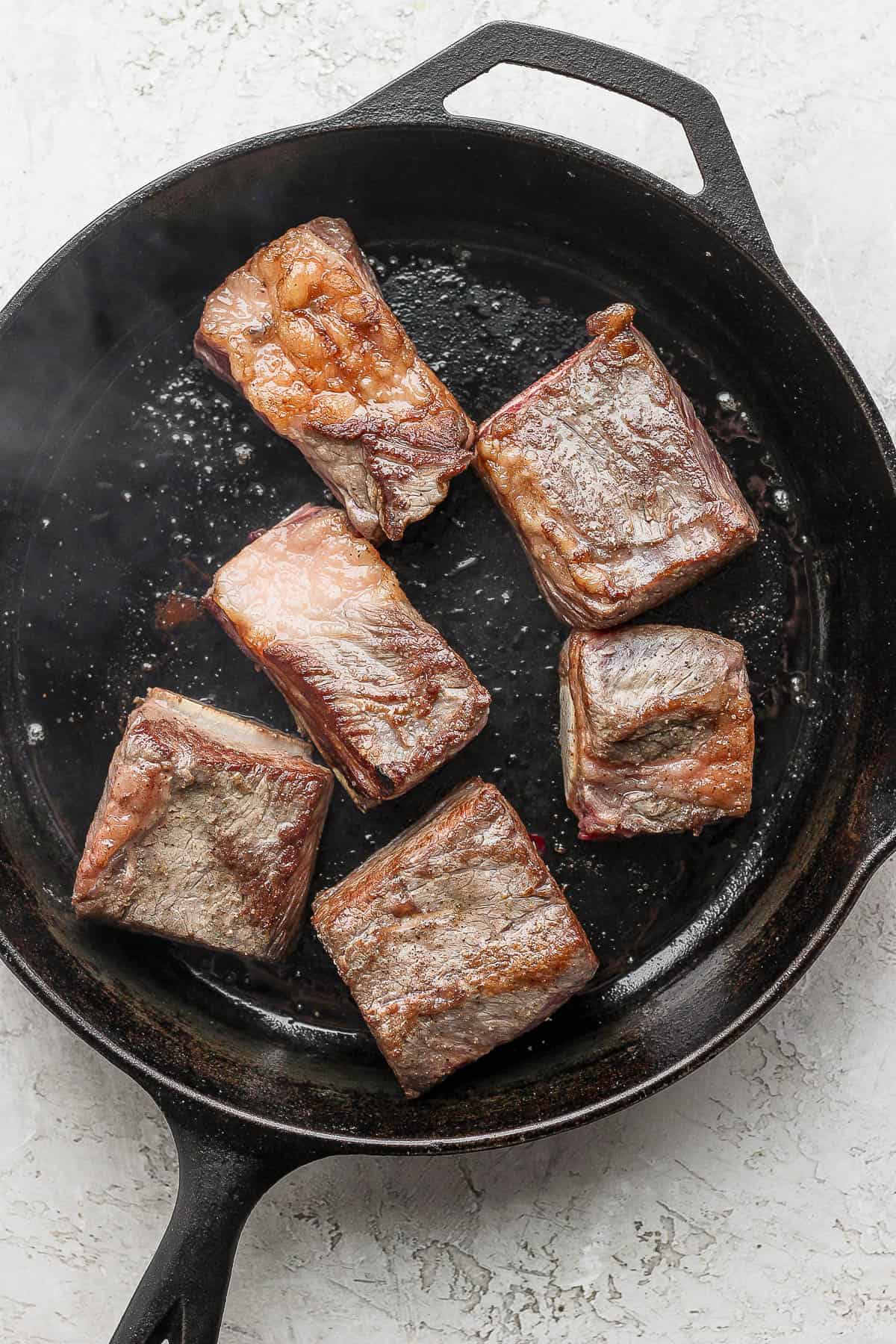 Short ribs being seared in a cast iron skillet. 