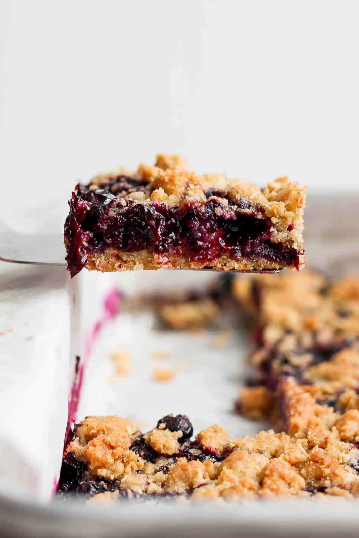 A blueberry crumb bar being lifted out of the pan.