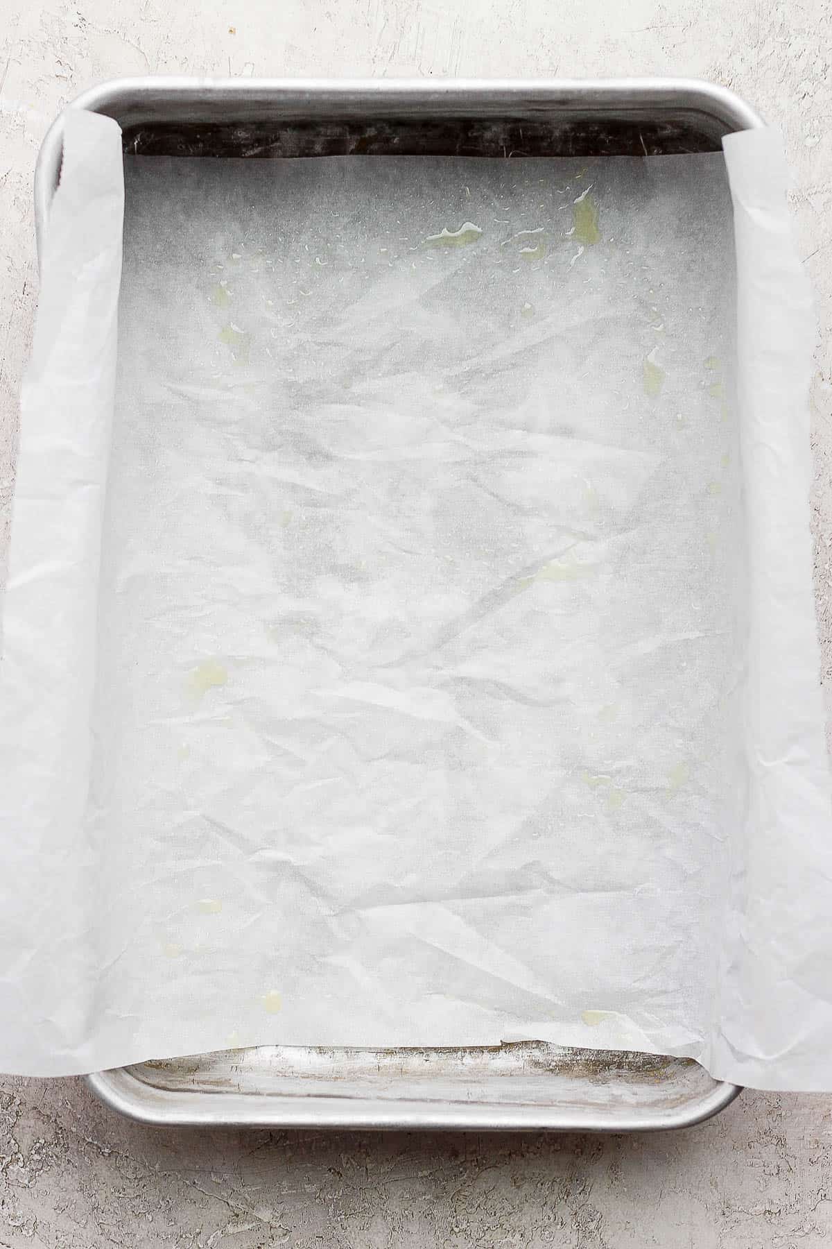 A metal baking pan with parchment paper that has been sprayed with cooking spray.