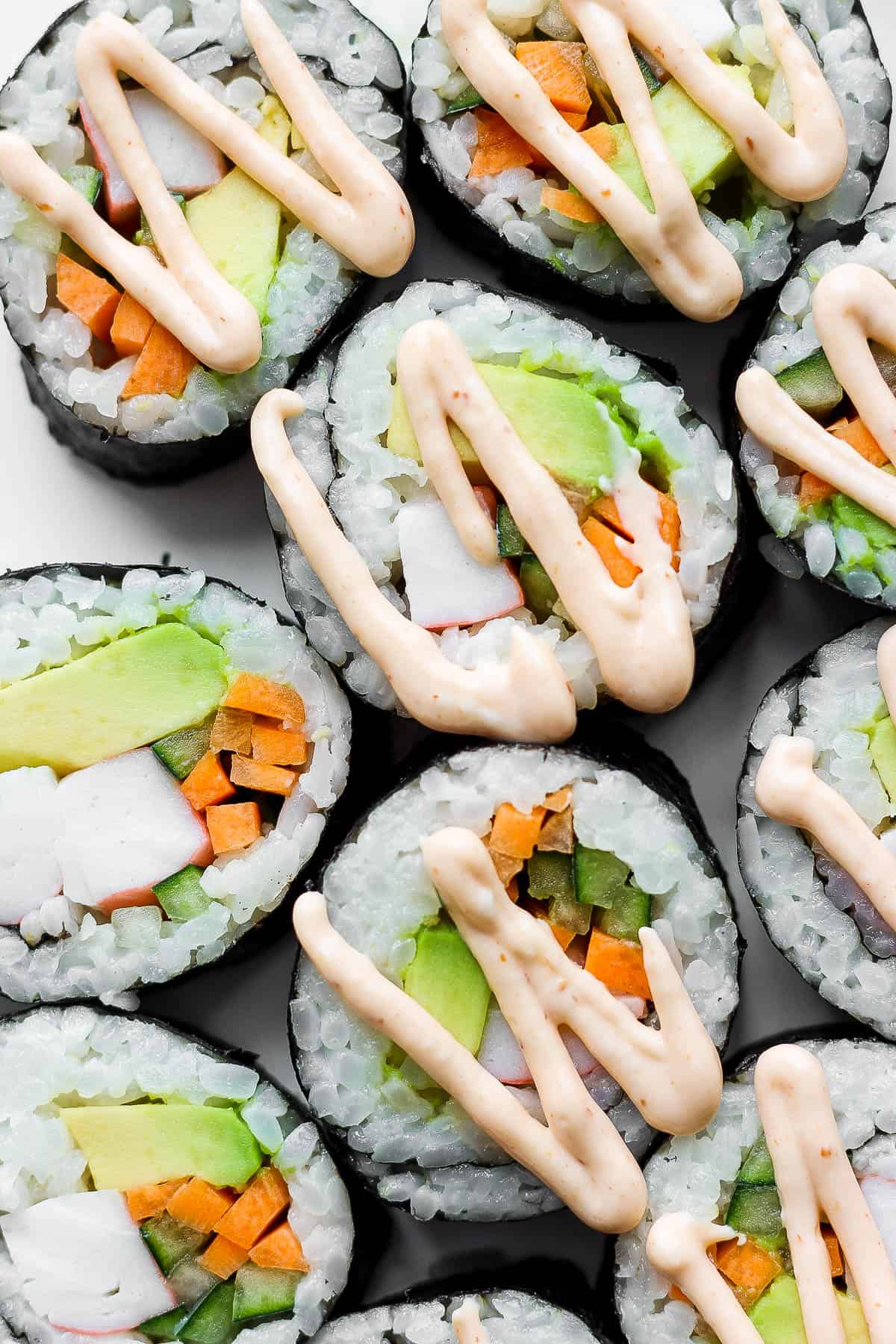 Pieces of a California roll on a white plate with spicy mayo drizzled on top.