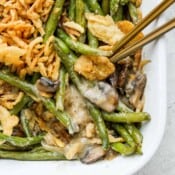 Close up shot of the corner of a pan of homemade green bean casserole with fresh green beans with two spoons sticking out.