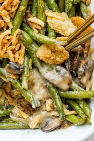 Close up shot of the corner of a pan of homemade green bean casserole with fresh green beans with two spoons sticking out.