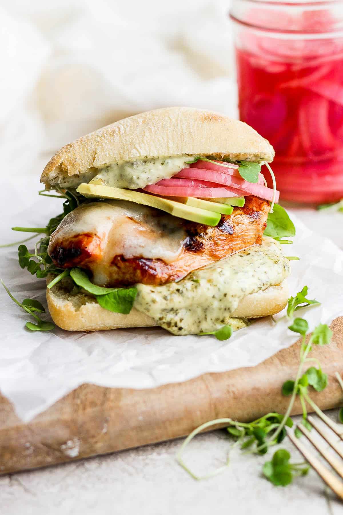 A grilled chicken sandwich on a plate with a jar of pickled onions in the background.