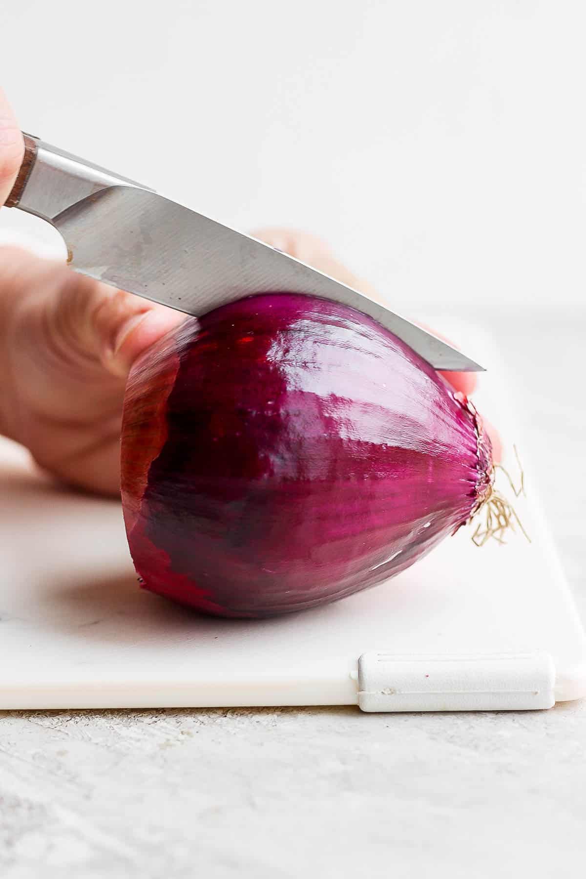 A large red onion being cut in half, lengthwise.