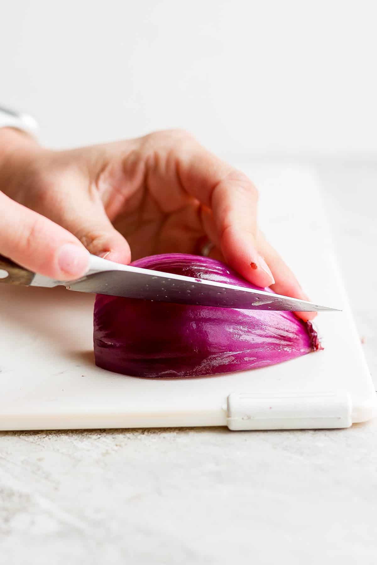A quarter of a red onion being cut into wedges.