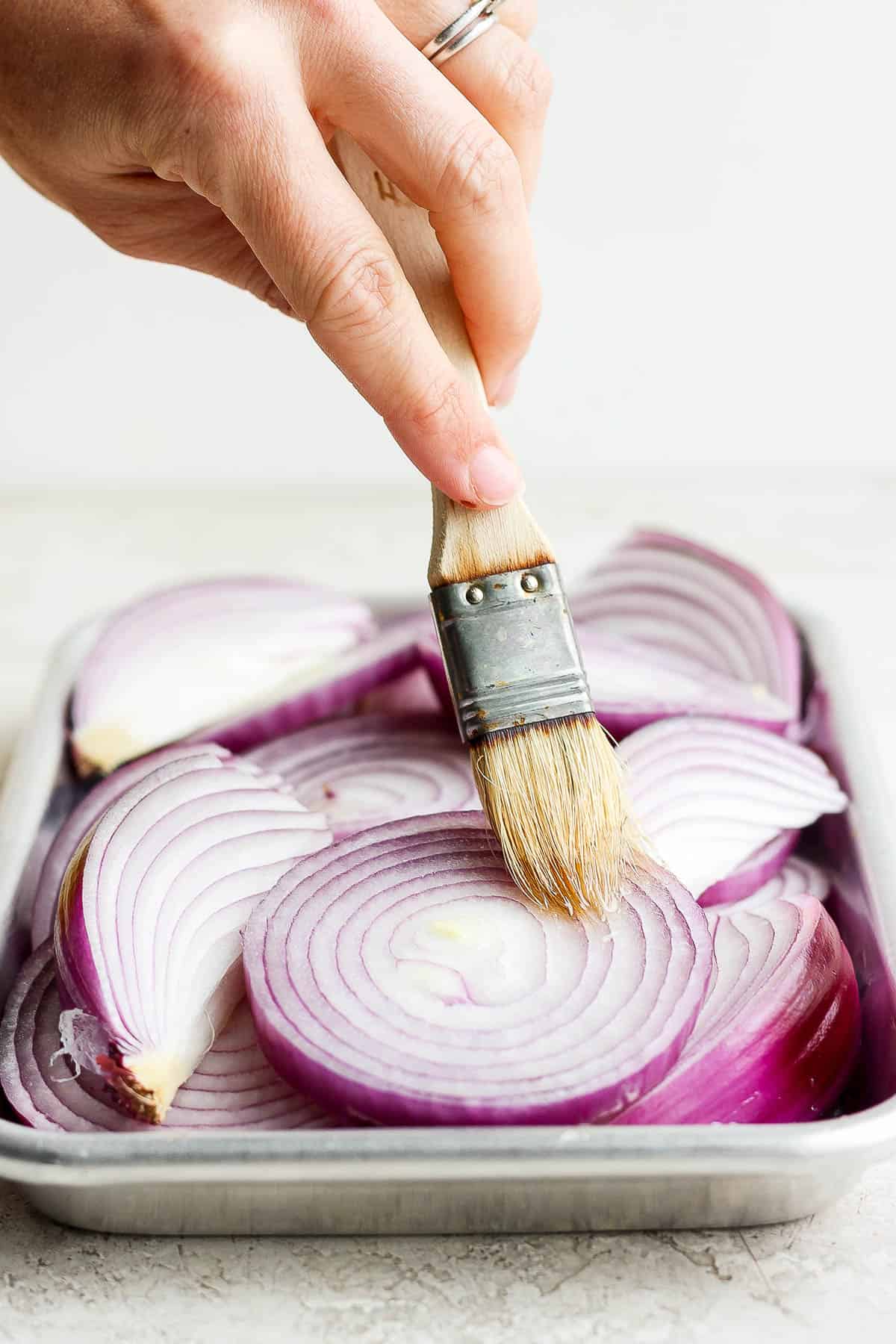 Onion slices and wedges being brushed with olive oil.