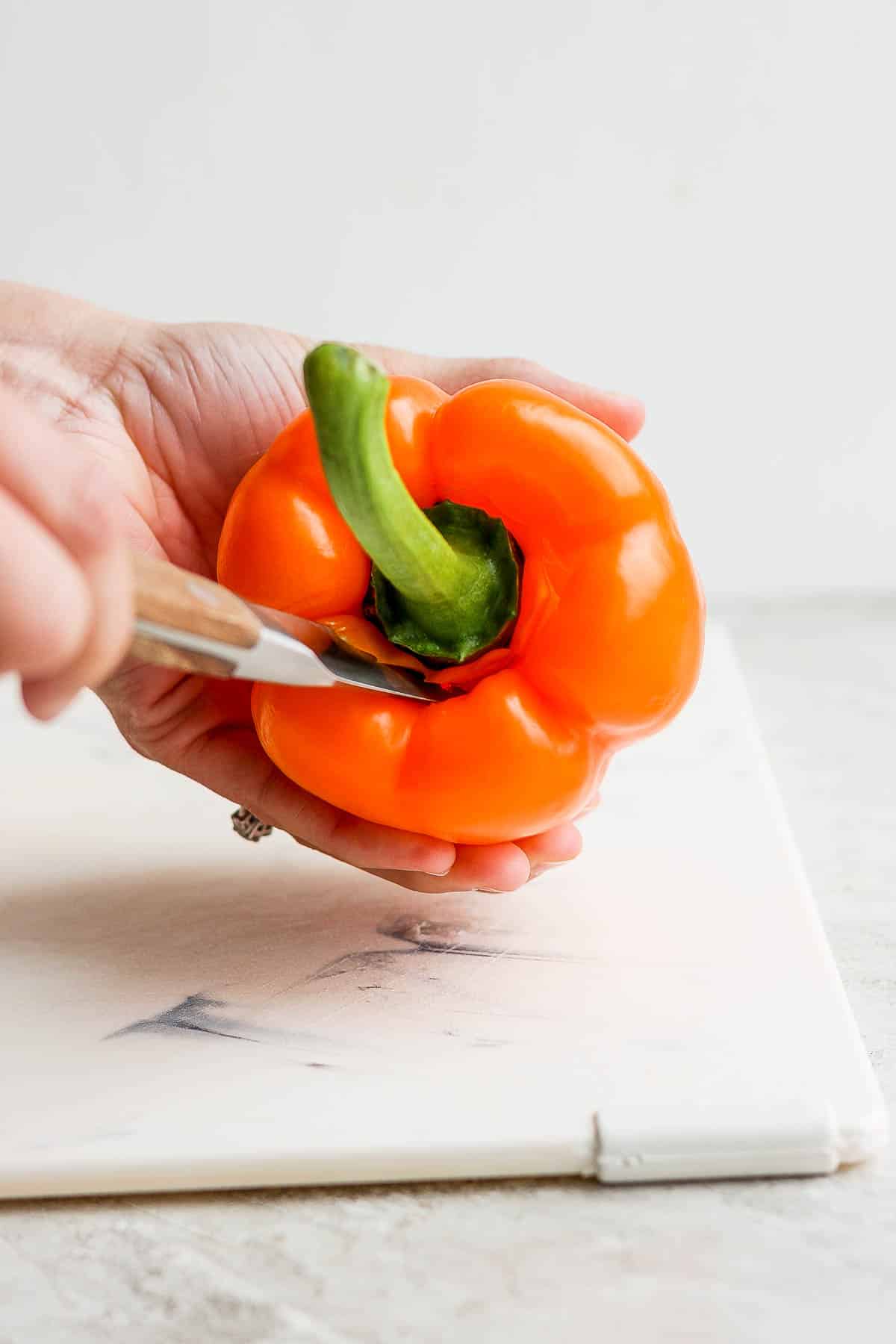The top of the pepper being cut out with a paring knife.