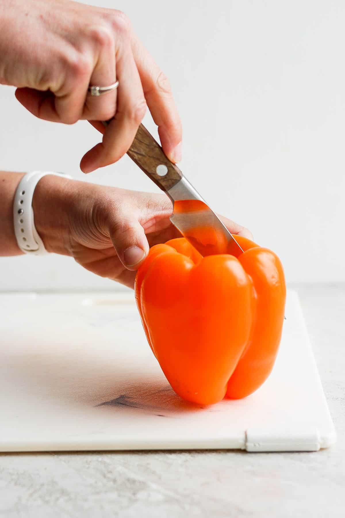 A knife cutting a bell pepper in half, lengthwise.
