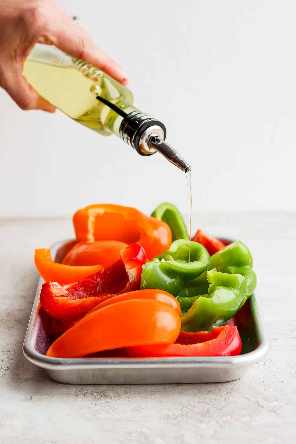 Olive oil being poured over quartered pieces of bell pepper.