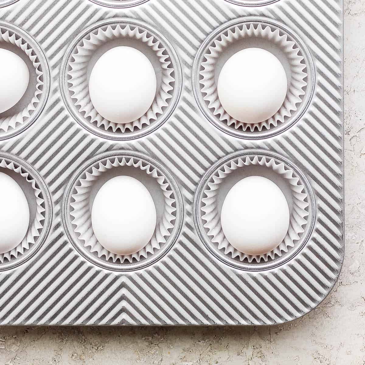 Six eggs sitting in muffin tins with muffin liners.