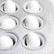 Six eggs sitting in muffin tins with muffin liners.