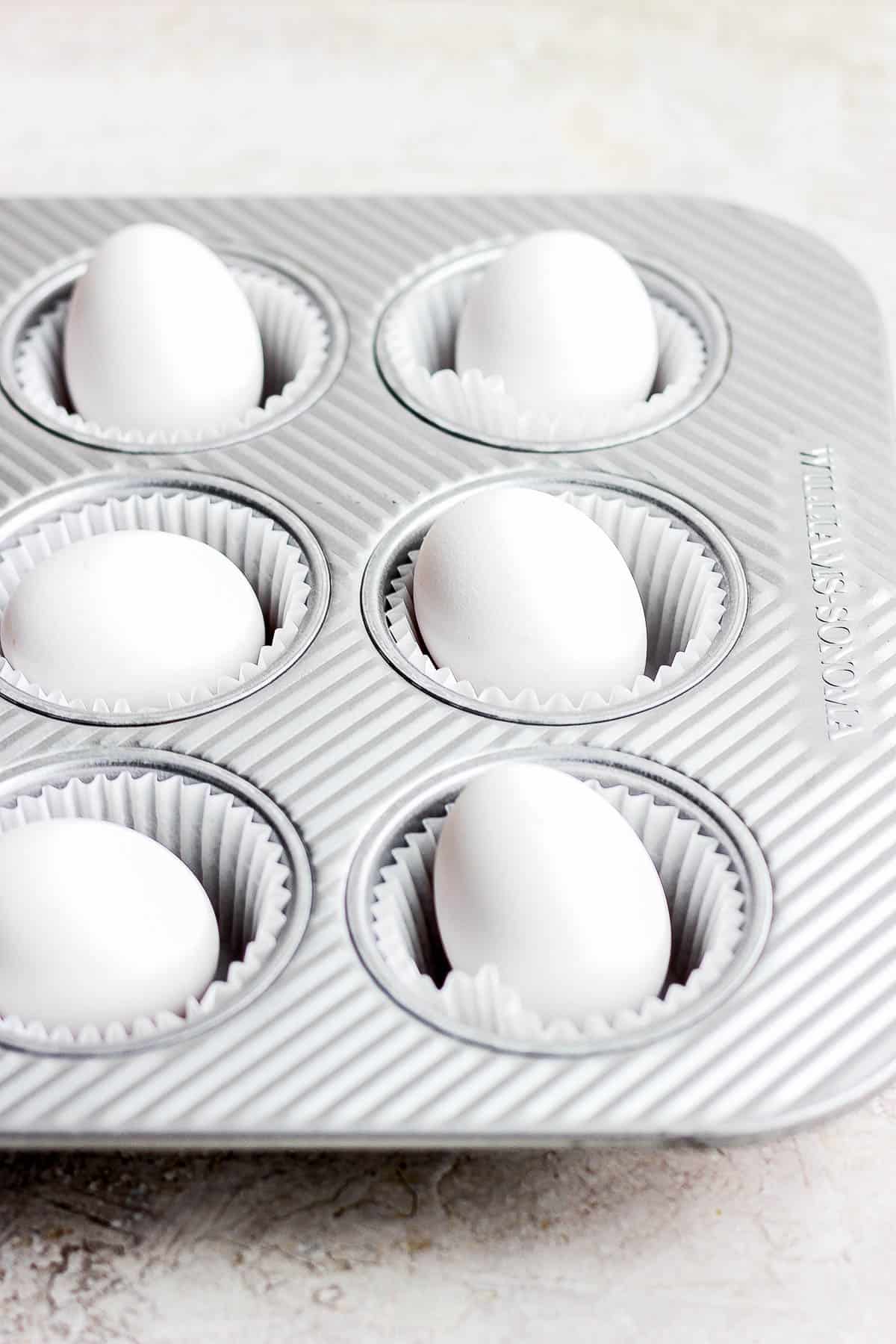 A muffin tin lined with muffin liners with an egg in each liner.