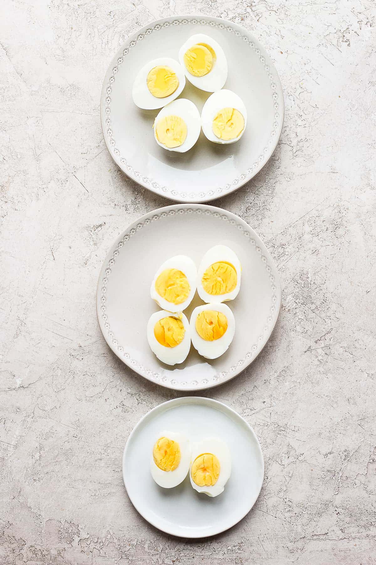 Three plates, in a line from the top to the bottom.  Each plate has two hard boiled eggs cut lengthwise, yolk side up.