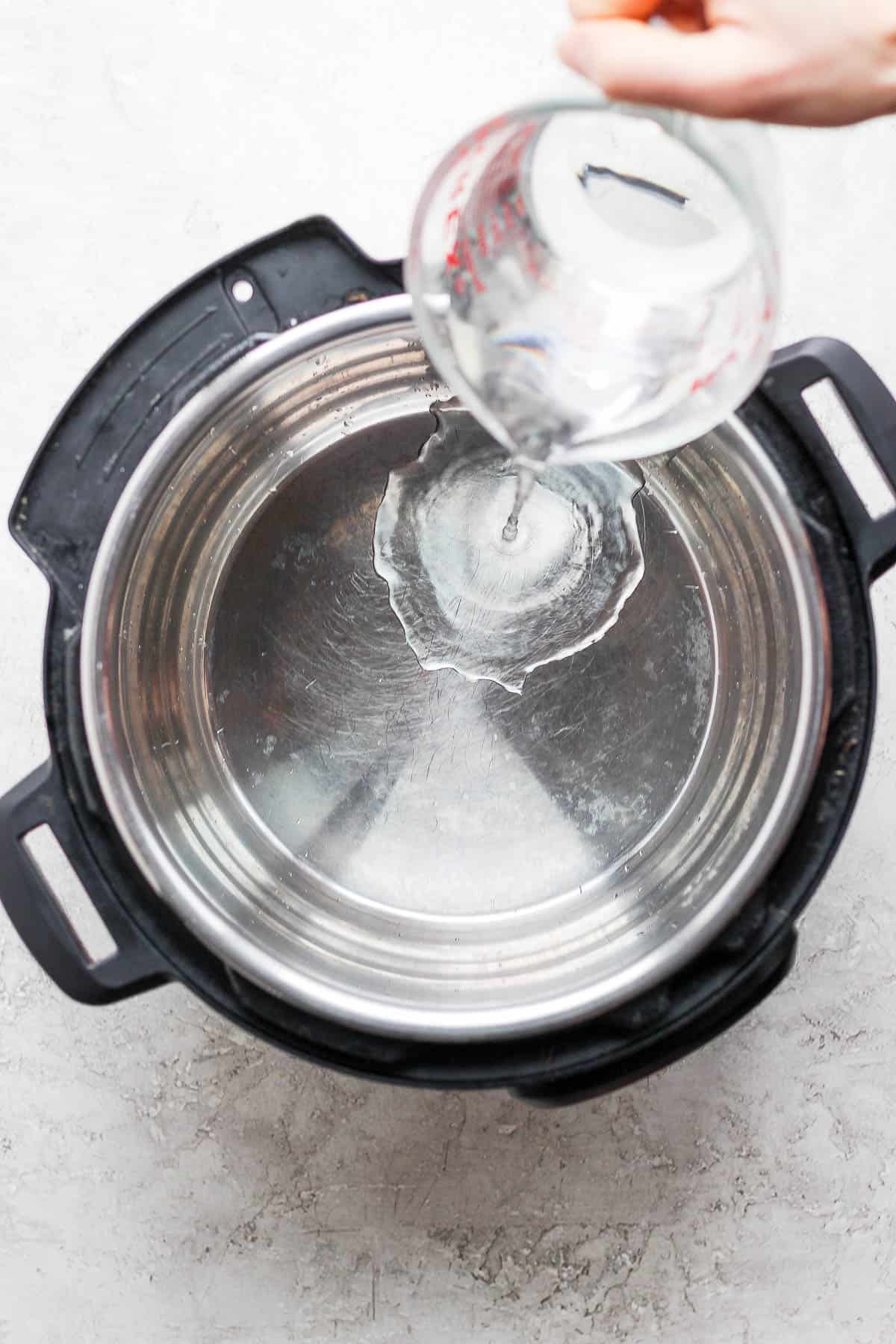 A measuring cup pouring a cup of water into an instant pot.