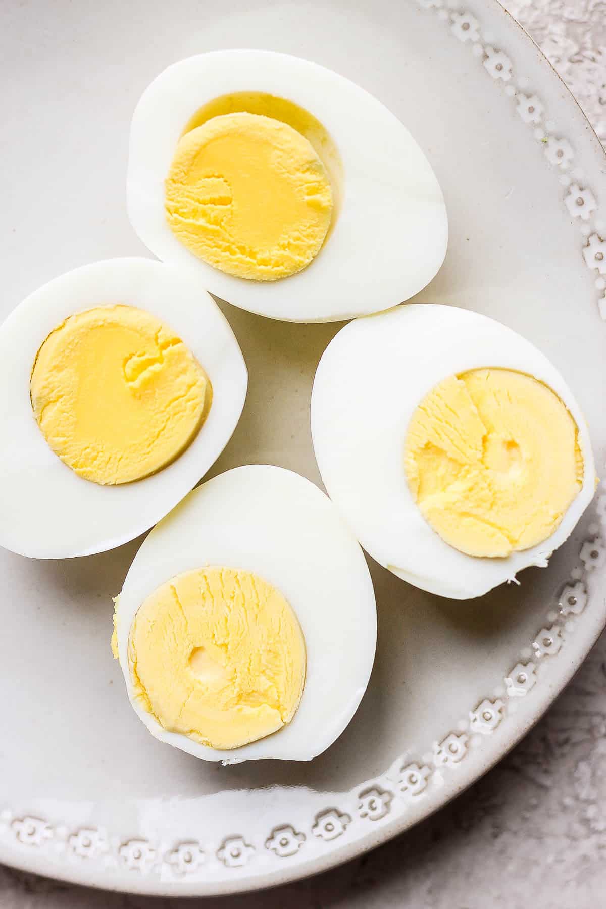 Two hard boiled eggs, cut lengthwise facing yolk side up on a plate.