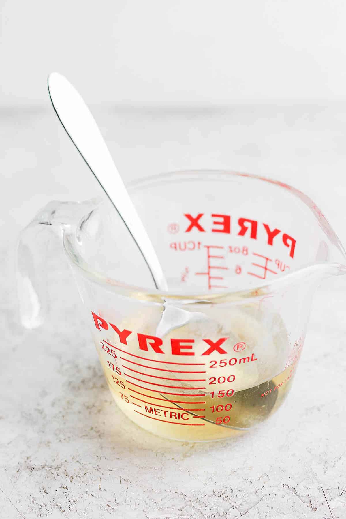 A glass measuring cup with the rice vinegar mixture and a spoon in it.