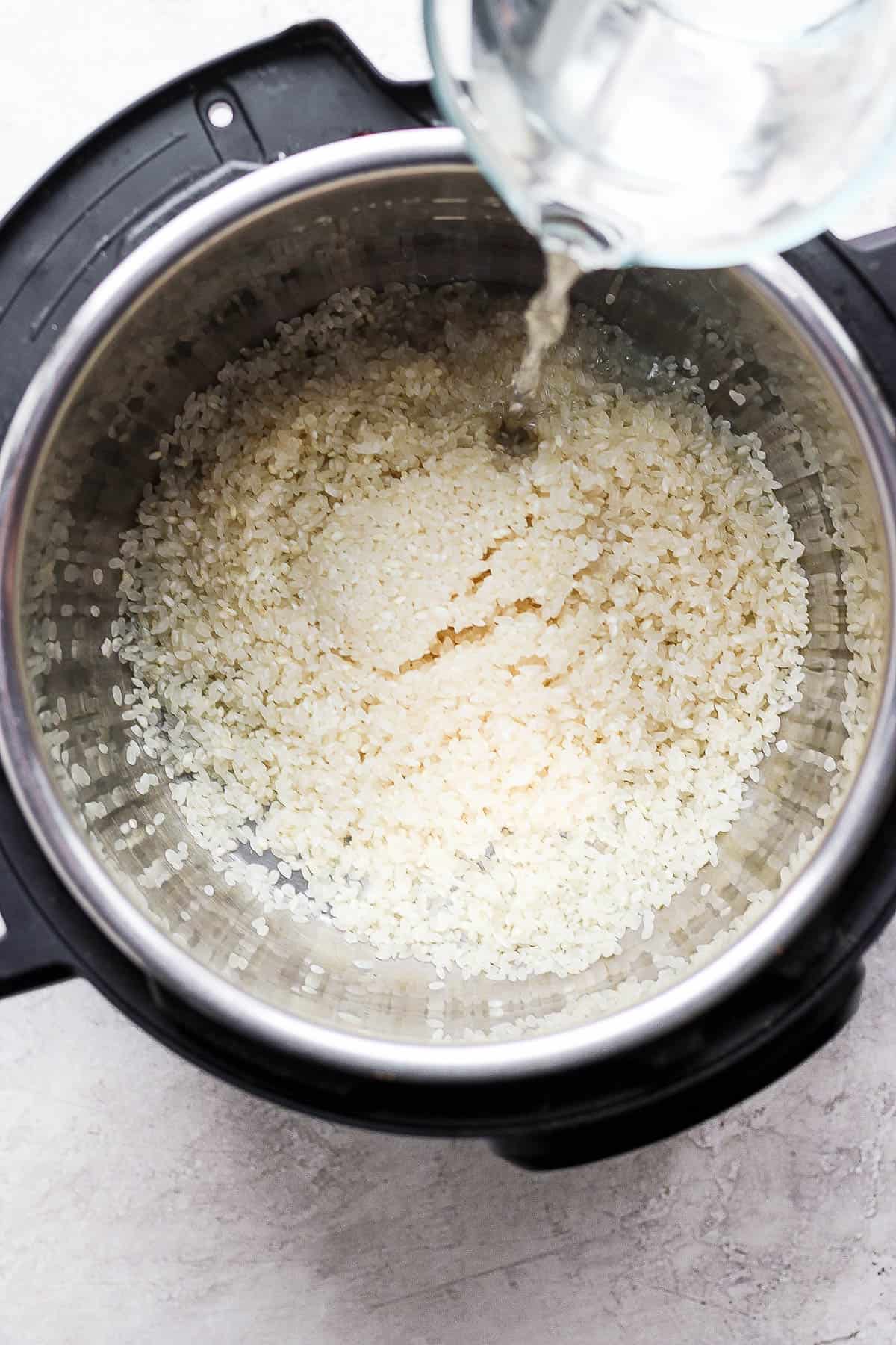 Rinsed rice in an Instant Pot with water being added.