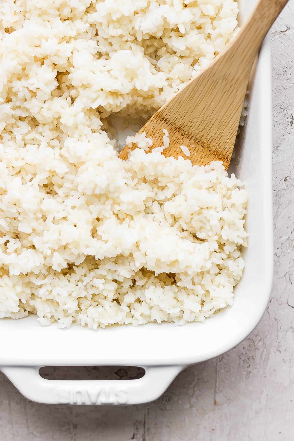 Sushi rice in a baking dish with a rice paddle.