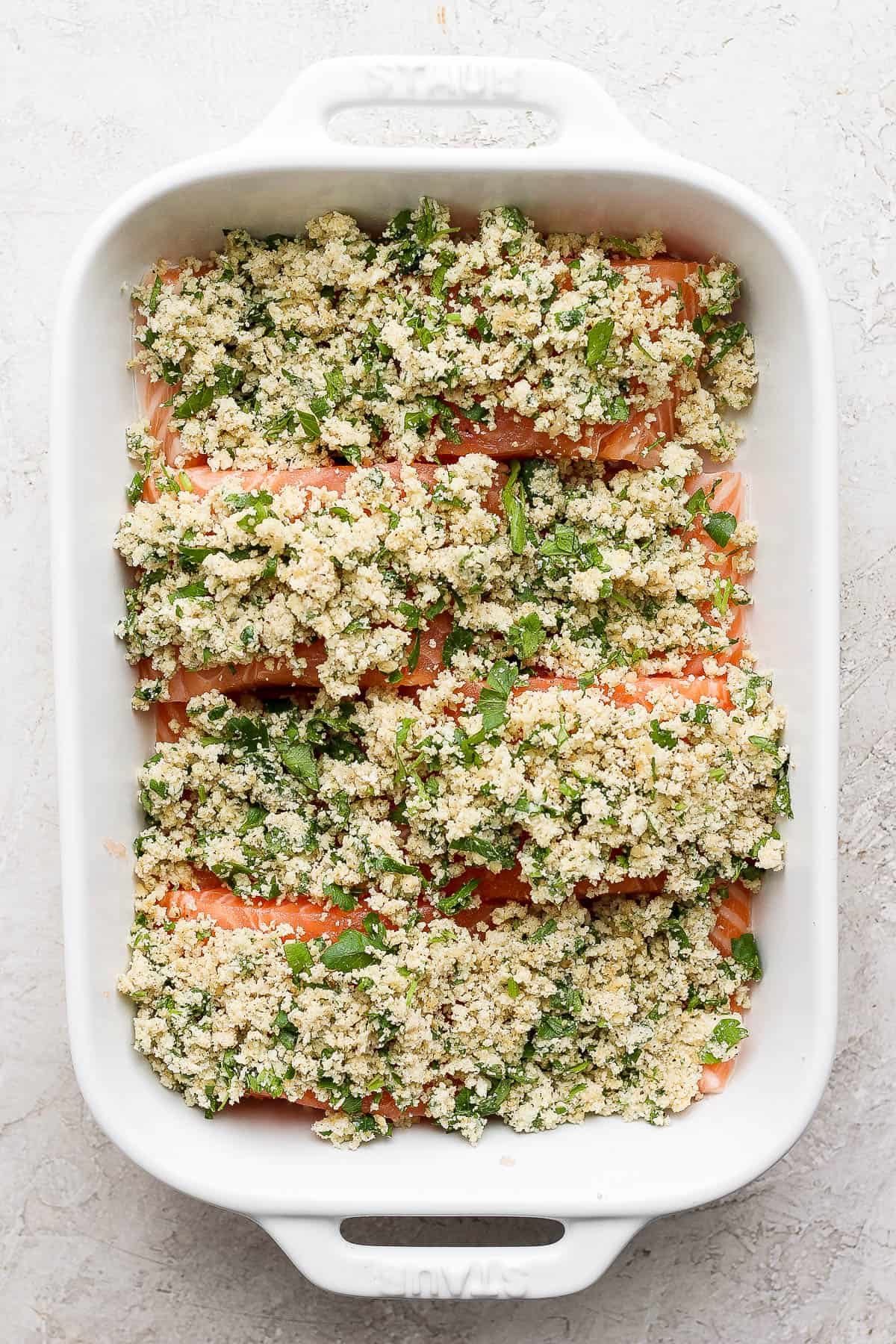 Four salmon fillets in a casserole dish topped with the panko seasoning mixture. 
