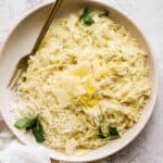 Top down shot of a bowl of parmesan orzo garnished with shaved parmesan and chopped parsley with a fork sticking out.