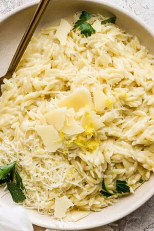 Top down shot of a bowl of parmesan orzo garnished with shaved parmesan and chopped parsley with a fork sticking out.
