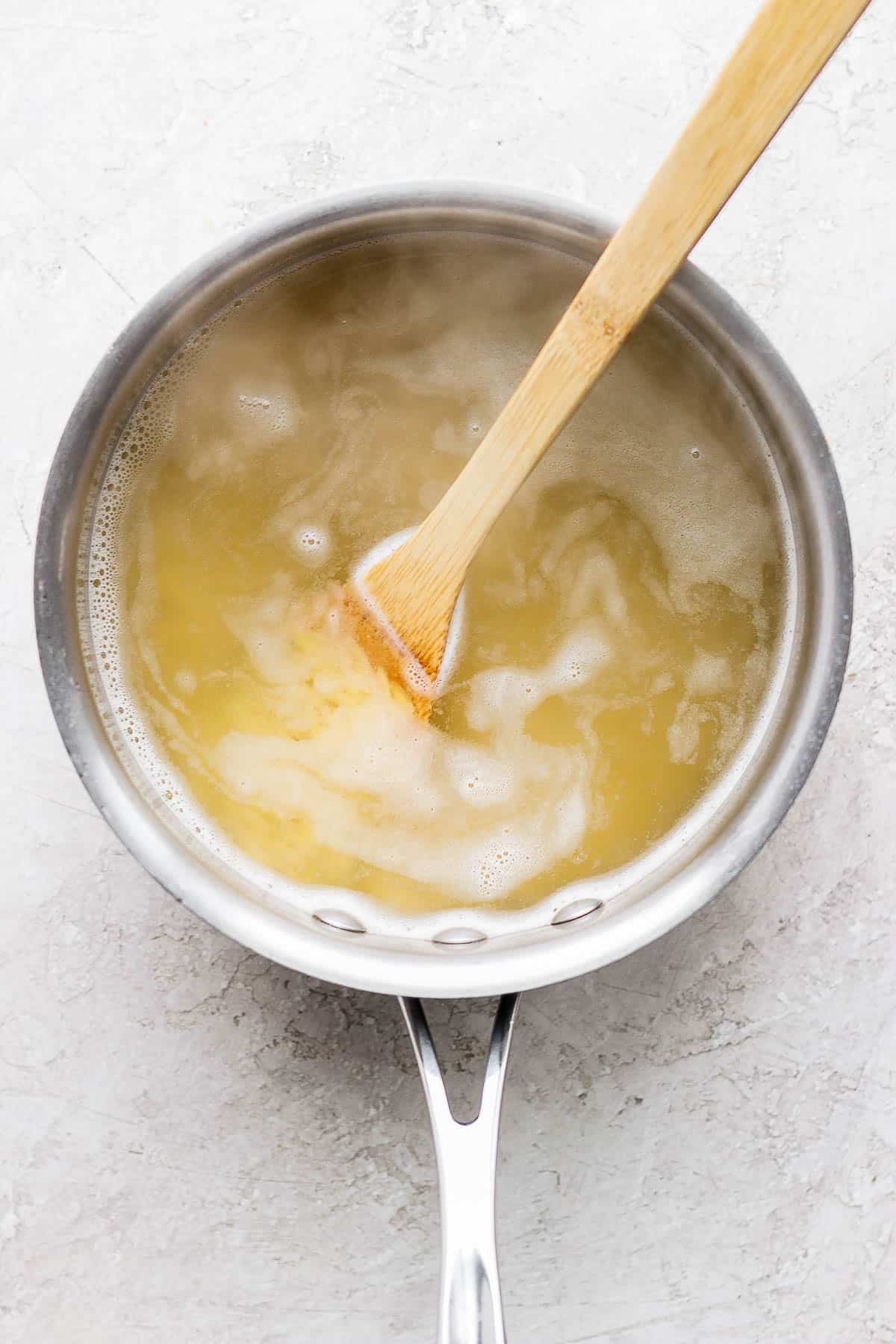 A medium sauce pan with boiling water, orzo, and a wooden spoon.