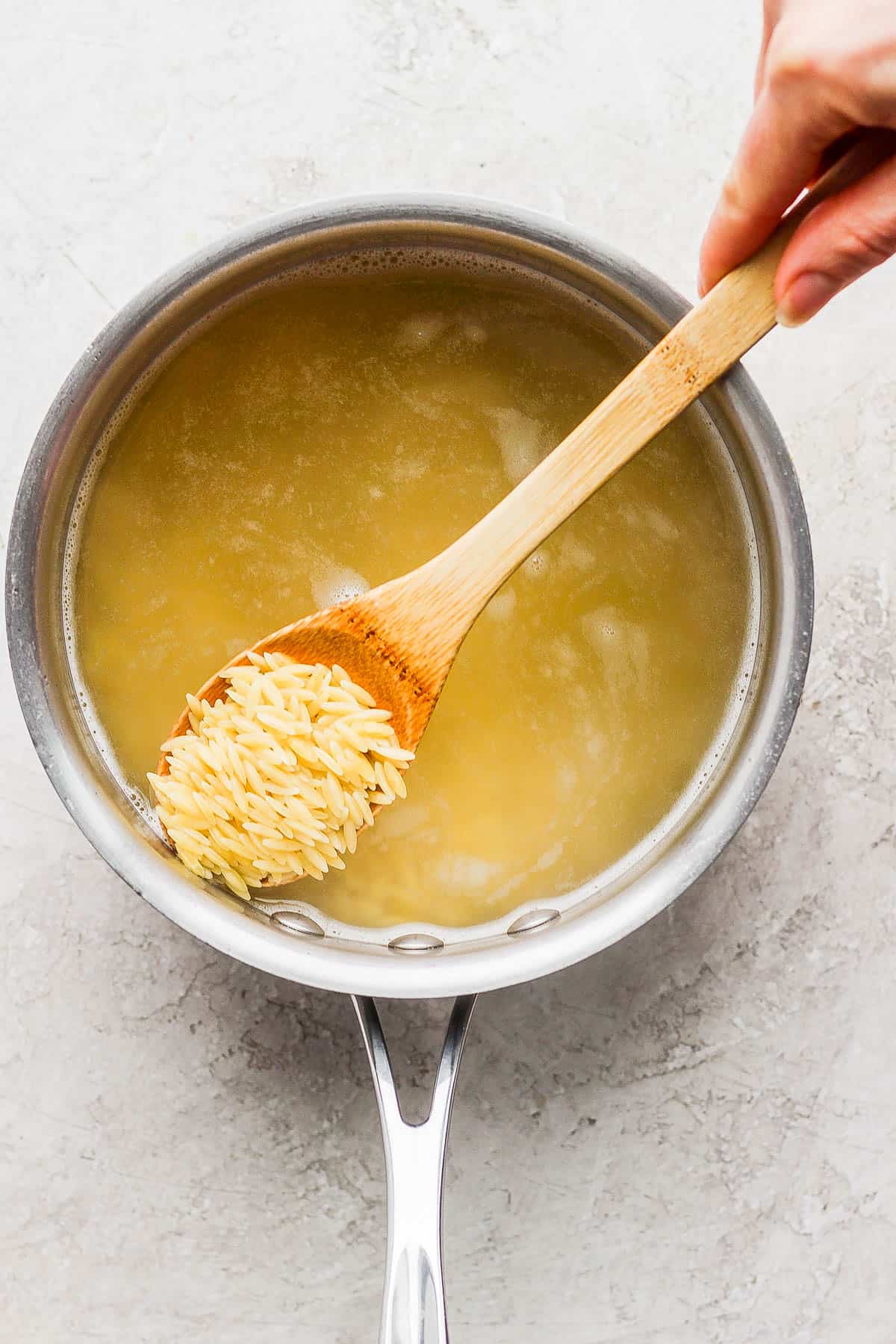 A spoon pulling cooked orzo out of the medium sauce pan.