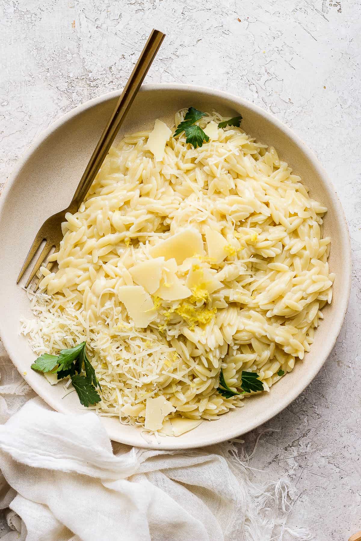 Parmesan orzo on a plate topped with parmesan cheese, lemon zest, and garnished with parsley.
