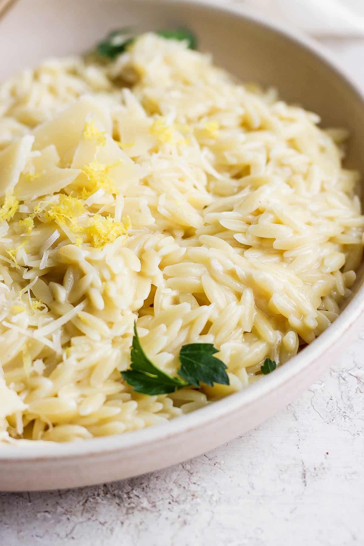 Parmesan orzo in a bowl garnished with lemon zest and parsley.