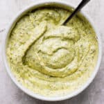 Top down shot of a bowl of pesto aioli with a spoon sticking out.