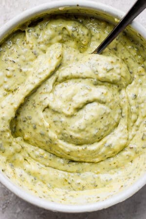 Top down shot of a bowl of pesto aioli with a spoon sticking out.