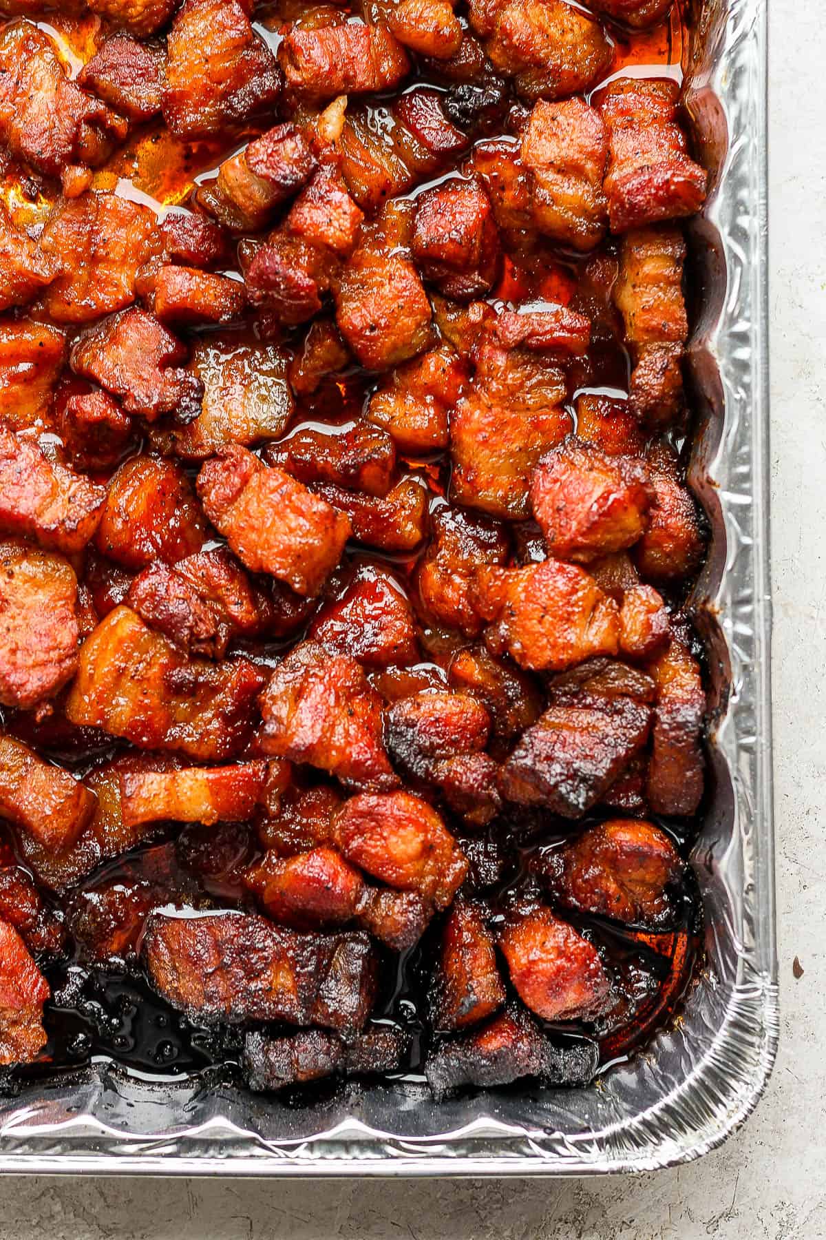 Fully cooked pork belly burnt ends in an aluminum tray.