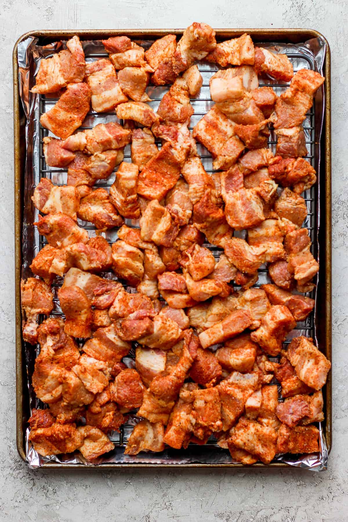 Seasoned pork belly pieces on a wire rack on top of a foil-lined baking sheet.