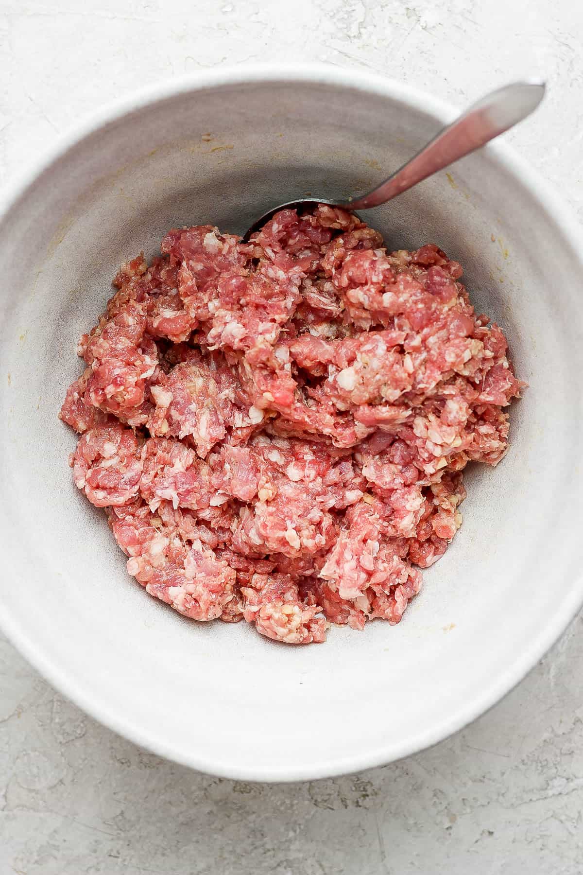 Pork burger ingredients all mixed together in a mixing bowl with a spoon.