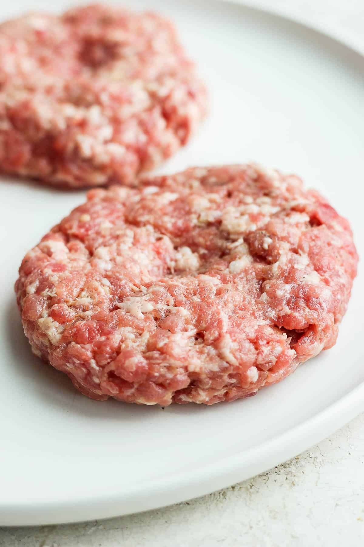 Pork burger patties on a white plate before cooking.
