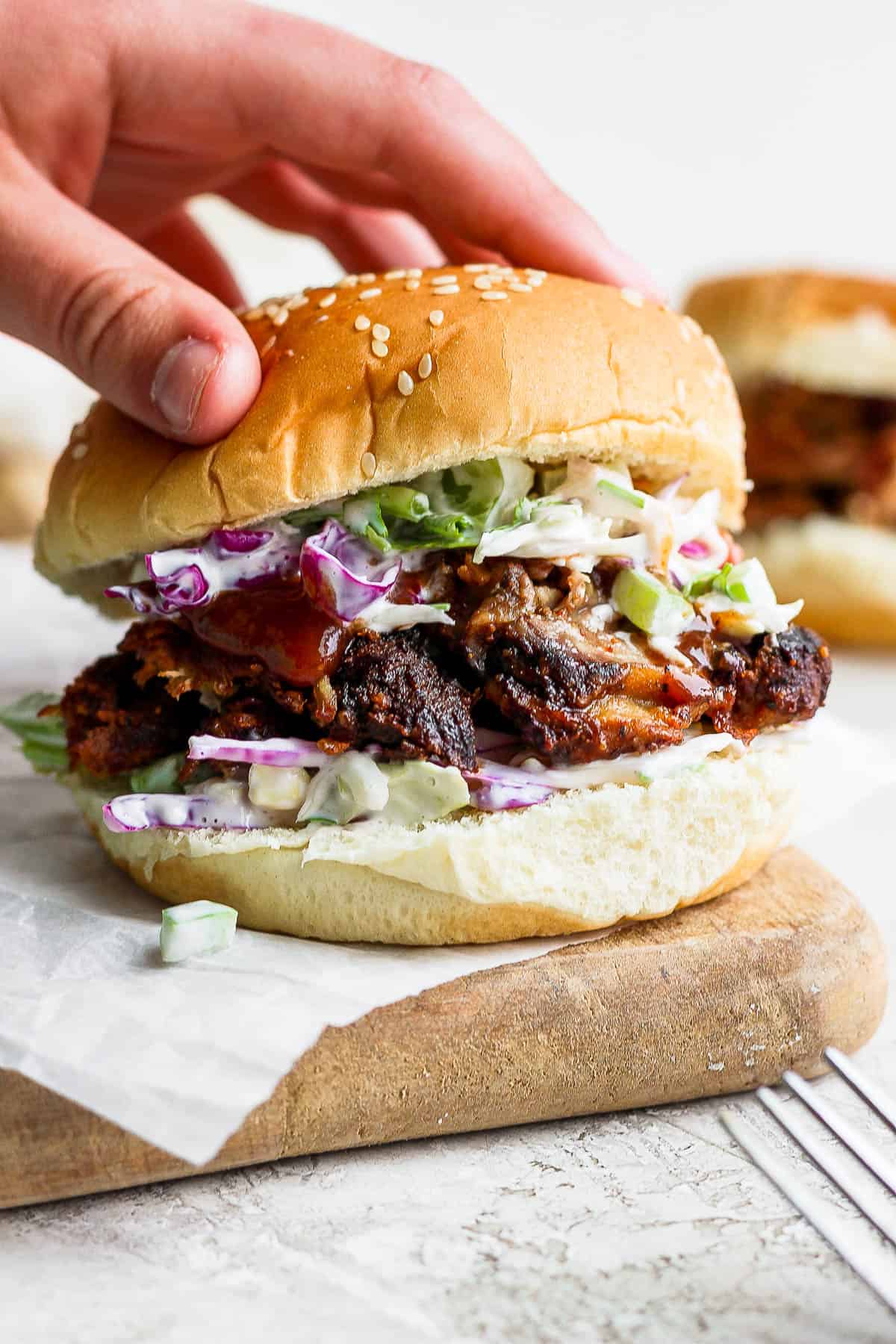 A hand placing the top of the bun on the sandwich.