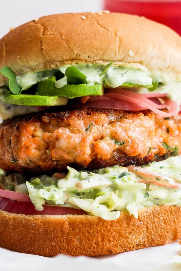 Straight on shot of a salmon burger on a bun with pickled onions, avocado and arugula.
