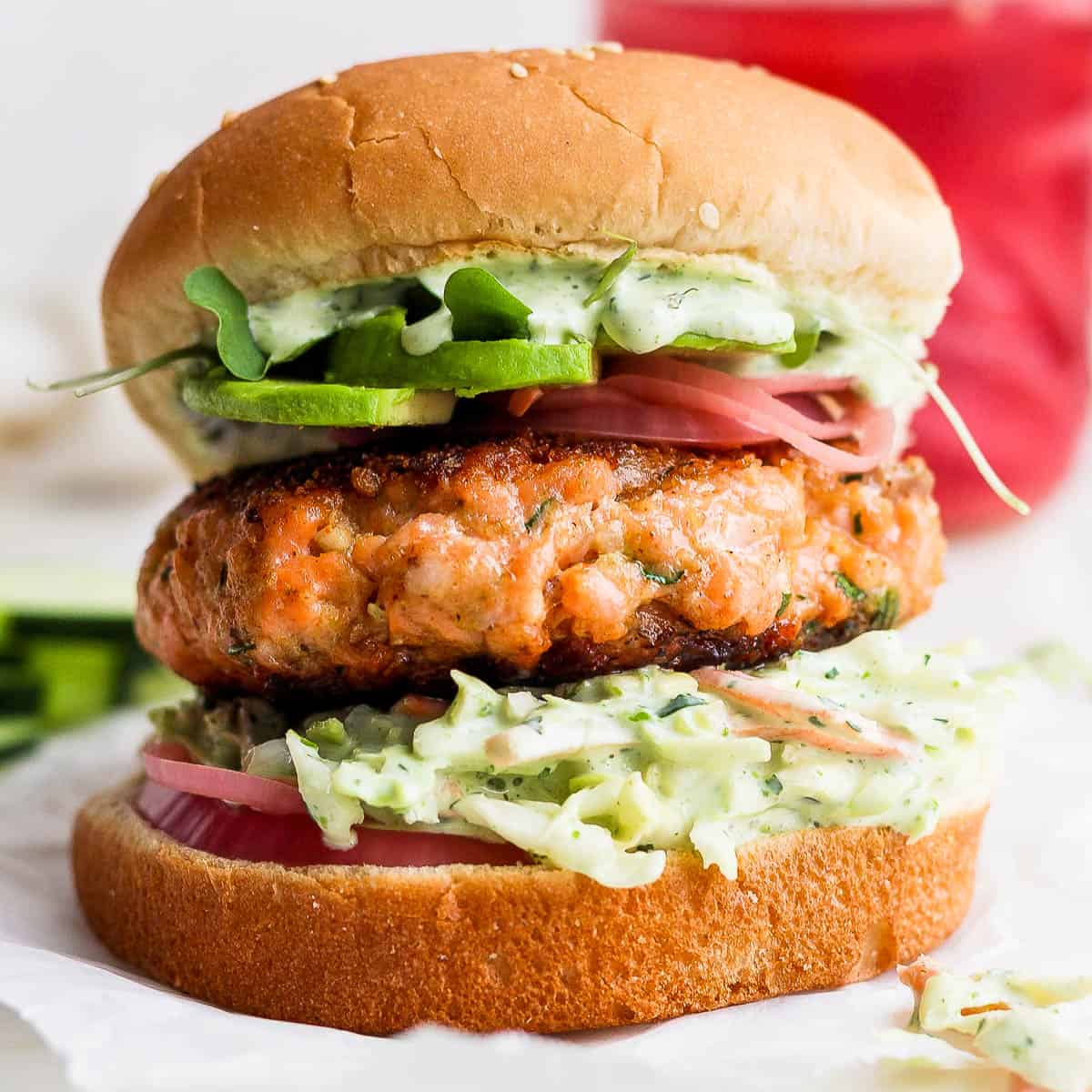 Straight on shot of a salmon burger on a bun with pickled onions, avocado and arugula.