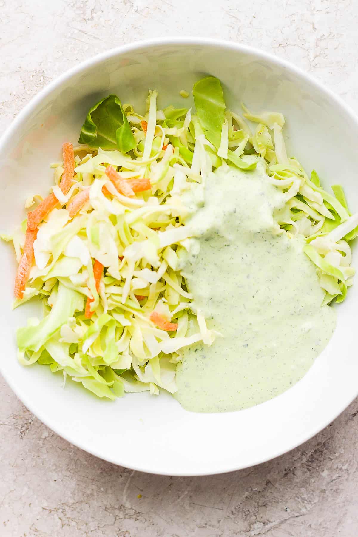 Coleslaw mixture in a bowl with some green goddess dressing.